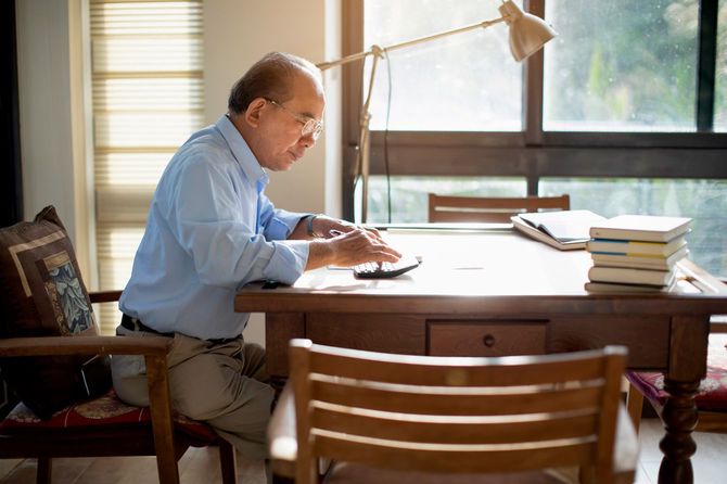 テーブルに座り電卓を使い、仕事するシニア男性