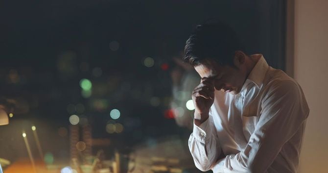 窓際で頭を抱えて悩む男性