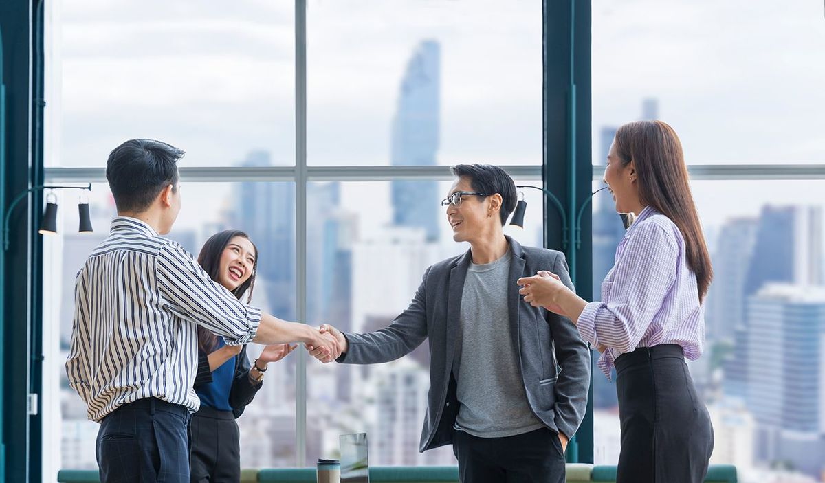 アジアのビジネスチームリーダーは、超高層ビルの景色を望む現代のオフィスワークプレイスで握手を交わすことによって、チームメイトの従業員の優れた業績チーム