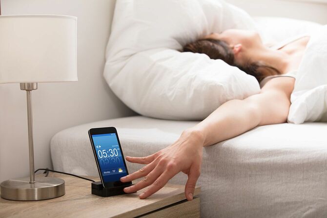 ベッドの上で携帯のアラームをオフにする女性
