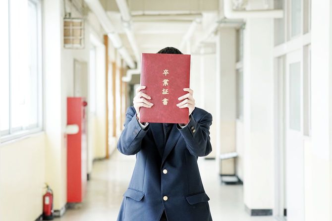 学校の廊下で卒業証書を持つ高校生