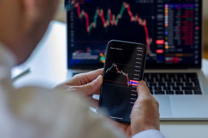 市場チャートをパソコンとスマホで開いて確認している男性の手元