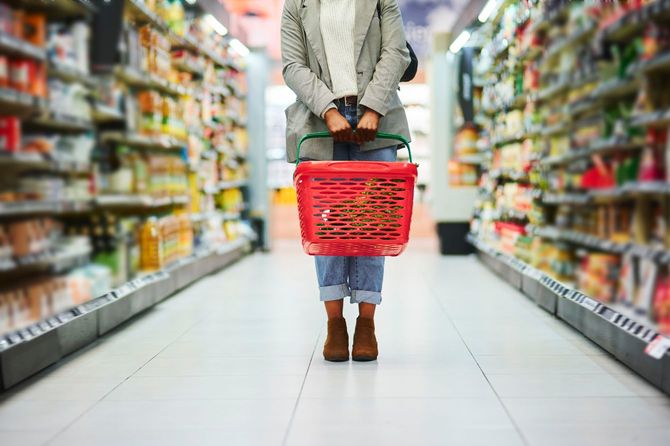 買い物かごを手に、スーパーの通路に立ち尽くしている女性