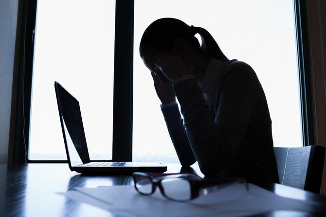 ノートパソコンの前でこめかみを押さえるストレスのたまった女性