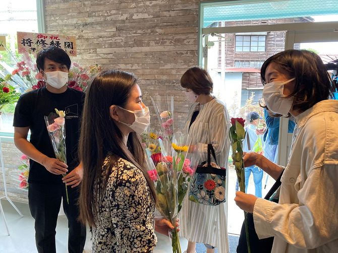 初日に来場のお客様一人ひとりに花を一輪ずつ渡す（手前左の女性がスタッフ。右の女性がお客さん左端が菊池氏