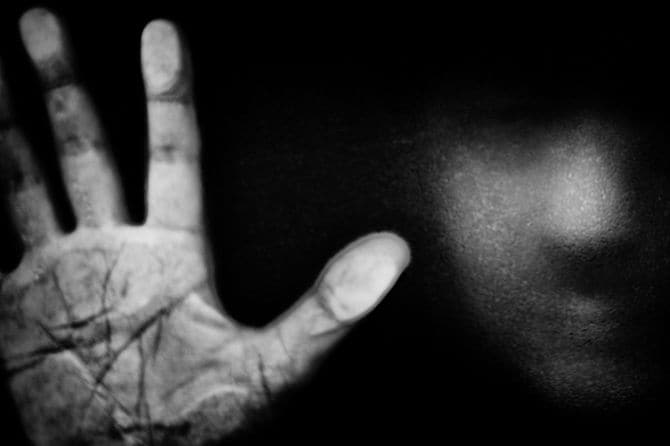 窓に手を当てて外を眺める人物