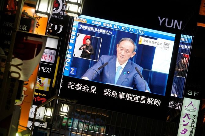 会見する菅義偉首相（当時）を映す街頭ビジョンと歌舞伎町の飲食店。