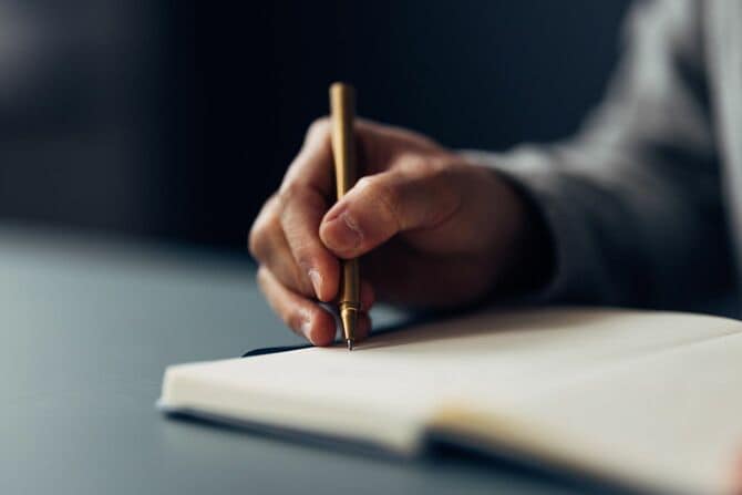 ペンでノートに手書きする手のクローズアップ