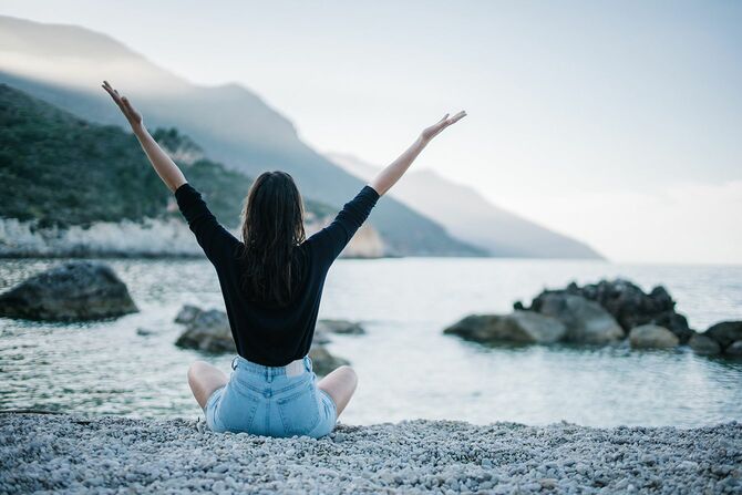 若い女性は日の出に岩のビーチで瞑想
