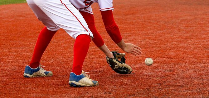 赤い芝生のフィールドにボールをフィールディングする野球の内野手