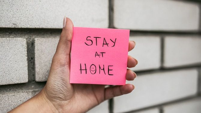 「おうちにいて」と書かれた紙を持つ女性の手