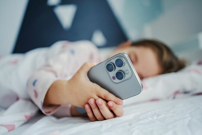 夜、スマートフォンを持ってベッドで寝る子供
