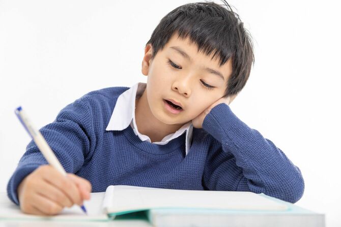 ストレスを抱えたアジア人の少年が家の机で勉強している