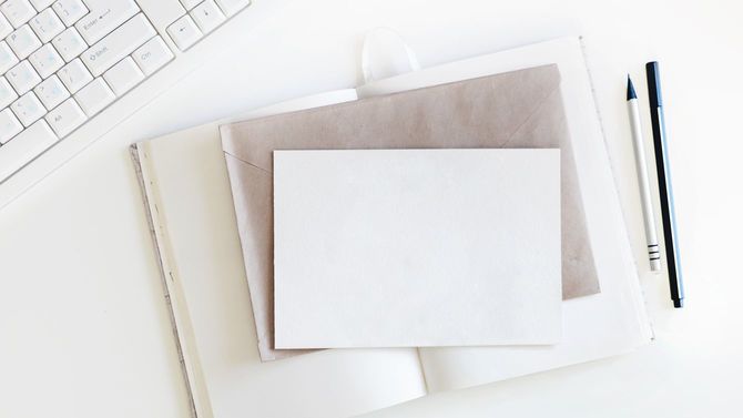 キーボードの手前に開いた手帳、その上に封筒、真っ白なはがき