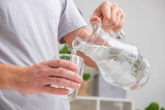 水差しからガラスのタンブラーに水を注ぐ男性の手