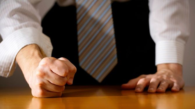 握りしめた拳で机をたたく男性