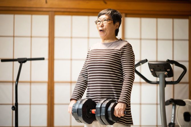 自宅でダンベルを持ってスクワットをするシニア女性