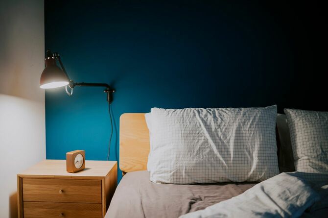 ランプによって照らされた青い壁の寝室とベッドサイドのテーブルの上の時計