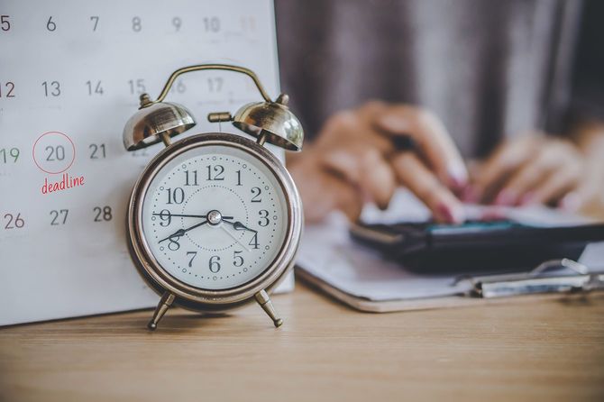 机の上の目覚まし時計とバックグラウンドで計算するビジネスウーマンをぼかして税金の支払いのための締め切りカレンダー