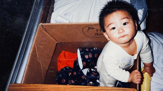 幼少期の笏本さん。工場の片隅に置かれた段ボール箱がベビーベッドがわりだった