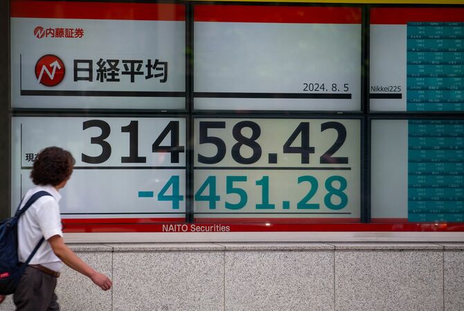 2024年8月5日、東京でリアルタイムの株式市場情報を表示するスクリーンを通過する歩行者。日経平均株価は12％以上下落し、下げ幅としては史上最悪となった。