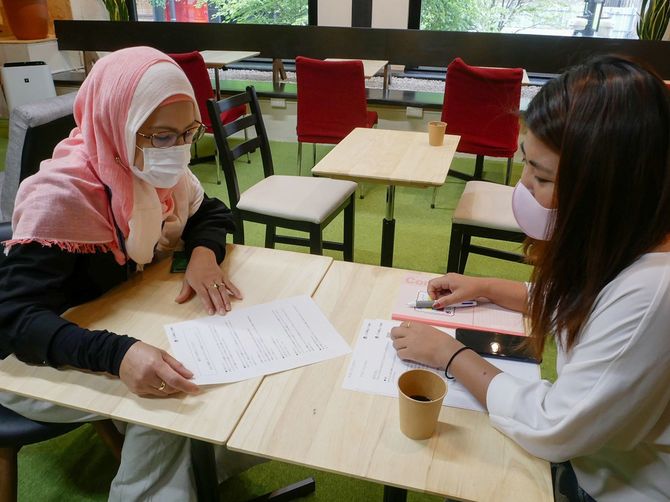 新型コロナウイルスに関する情報について、平易に書かれた資料を使って留学生に説明するインドネシア人スタッフ（左）