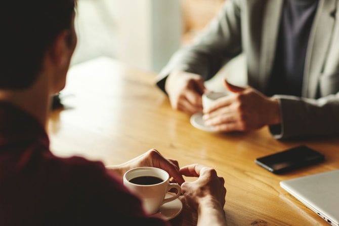 カフェのテーブルに座ってコーヒーを飲みながら話している2人