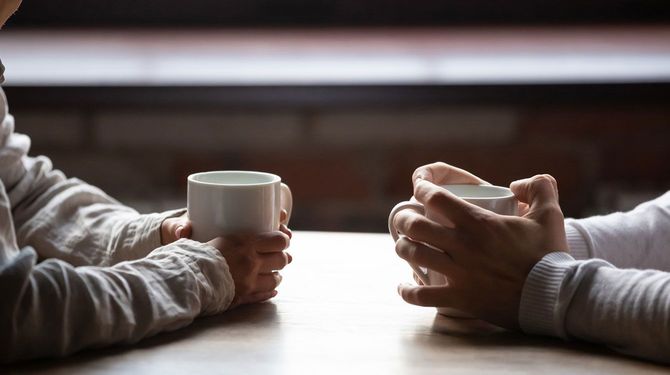 マグカップを両手で持ち、テーブルで向かい合う二人の手元