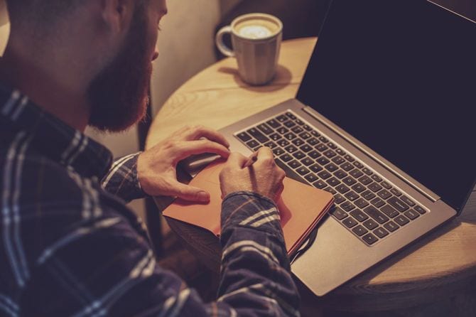 ノートパソコンの上にメモを開いて書き込んでいる男性