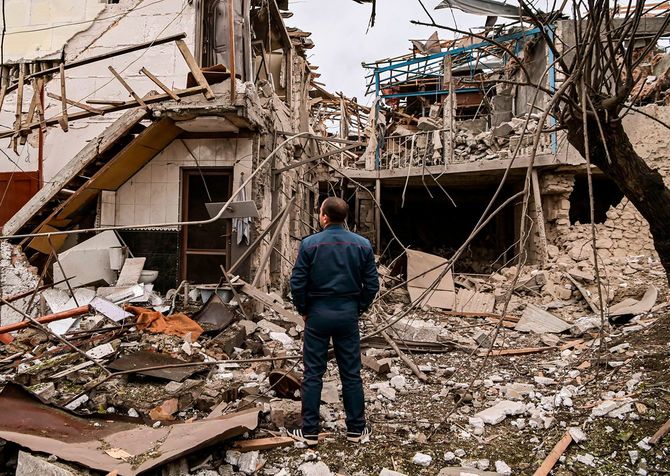 ナゴルノ・カラバフ地域の主要都市ステパナケルトで砲撃を受けた後、破壊された家屋の前に立つ警察官