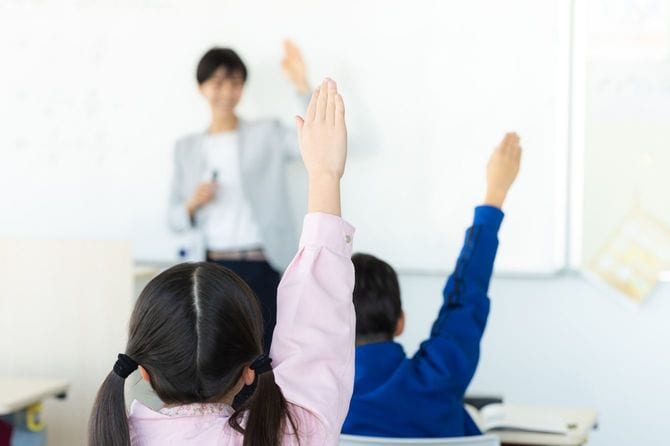 教室で手を挙げる小学生の授業風景