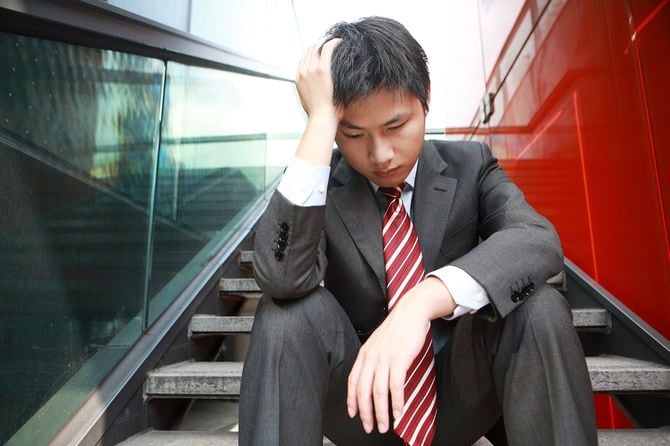 外階段で頭を抱える若いビジネスパーソン