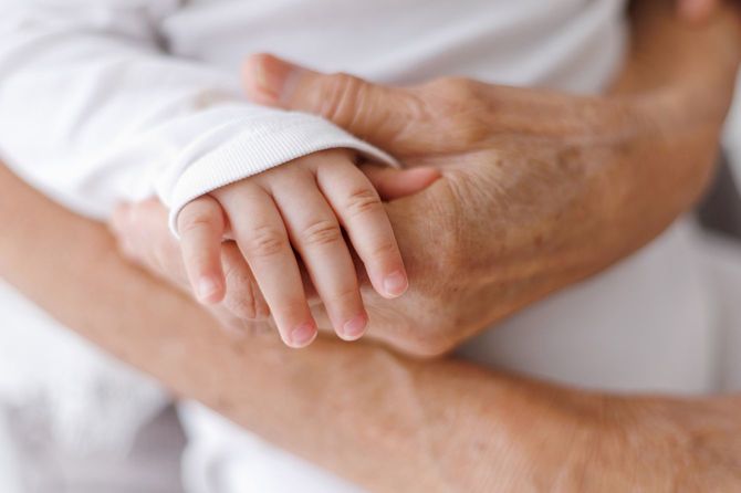 女の赤ちゃんの手を握る老婆の手が接写