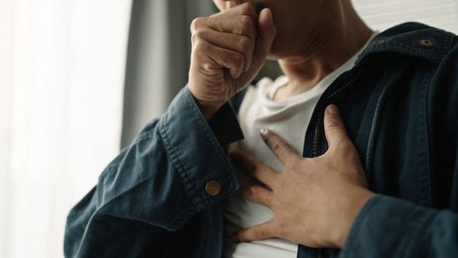 左手で胸を押さえながら咳をする男性