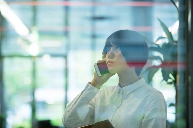 窓ガラスの向こうでスマートフォンで電話する女性