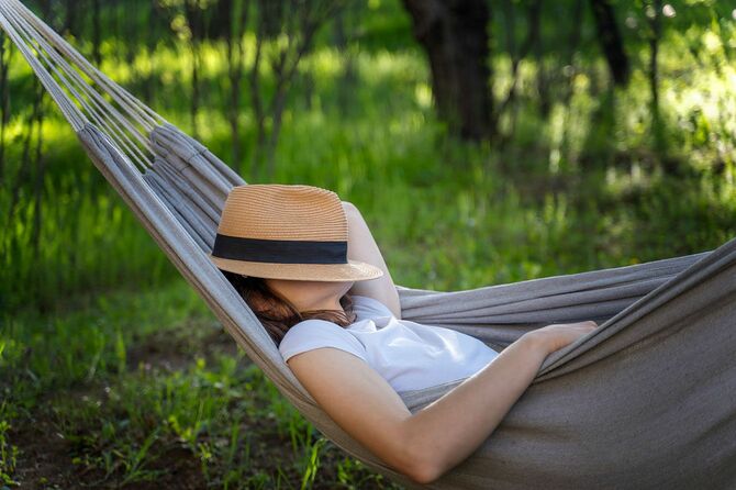麦わら帽子で顔を覆う夏の庭のハンモックで休む女性