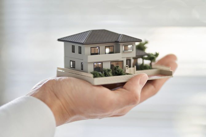 一軒の家の建築模型を持つアジア人男性の手