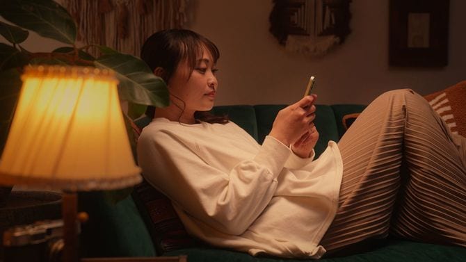 夜、ソファでスマートフォンを見る女性