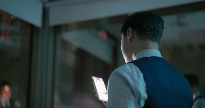 暗い部屋でスマートフォンを見るシニアビジネスマン