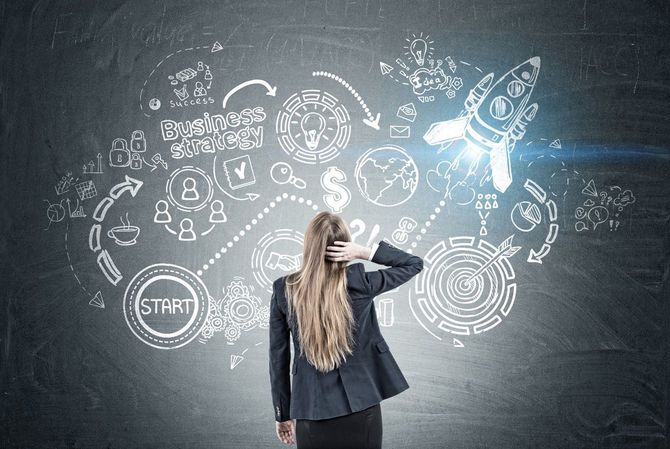 黒板に描かれたアイデアのスケッチを頭をかきながら眺めてい女性