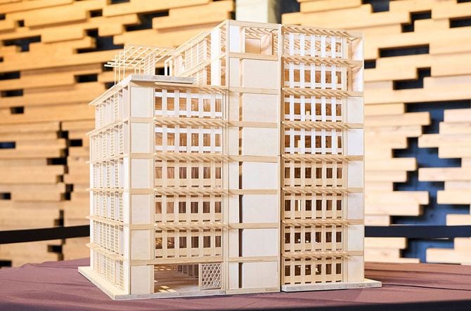 写真の模型は、2024年に「普及型純木造ビル」のプロトタイプとして完成した8階建てのAQ Group本社ビル（埼玉県さいたま市）。すでに普及している住宅用プレカット工場で製材、加工された木材を用いて、極力特殊な建築金物を使わずに造ることで各地の工務店や地場ゼネコンにも応用できる設計、施工の標準化を実現した。
