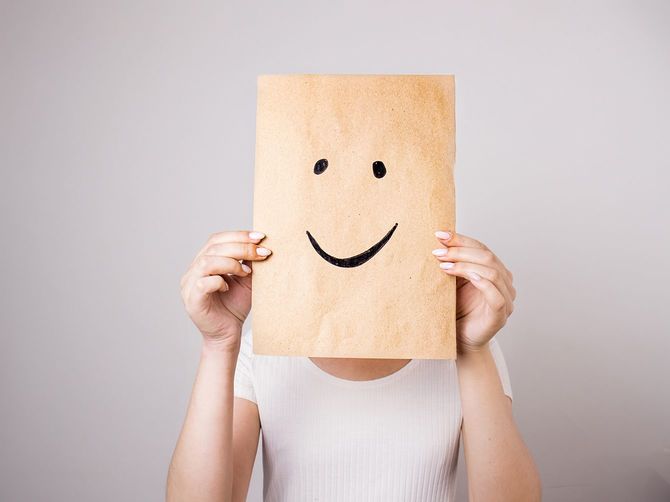 顔の前で絵のように塗られた笑顔で紙を持っている女性