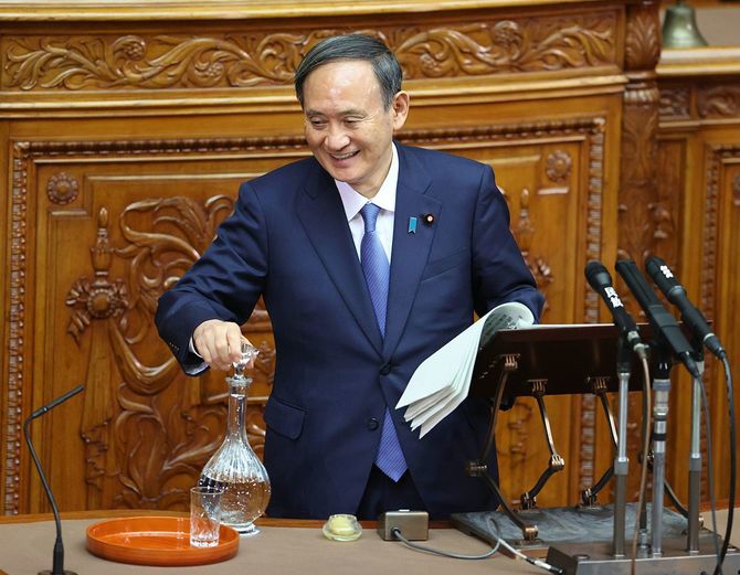 参院本会議での答弁中に、水差しの栓を外さずにグラスに水を注ごうとして苦笑する菅義偉首相