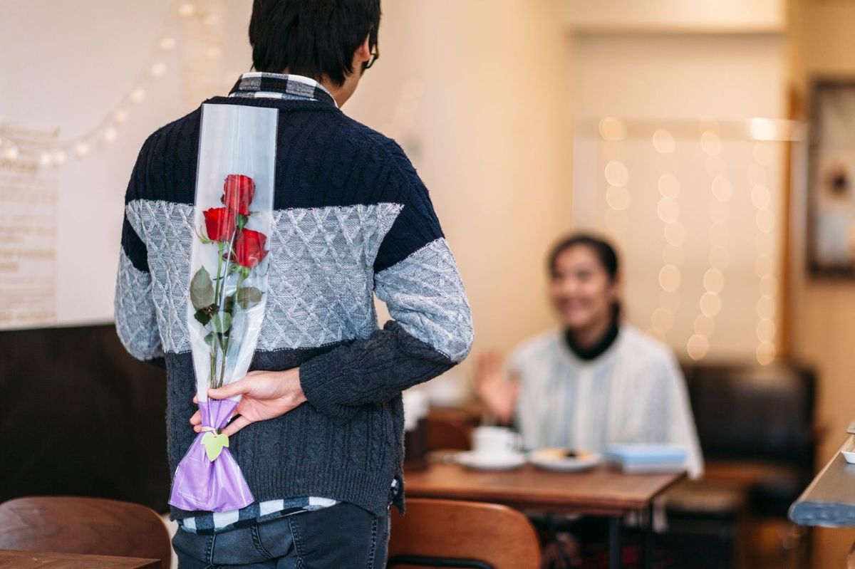 日本人男性がカフェでガールフレンドを驚かせるために花を隠している。