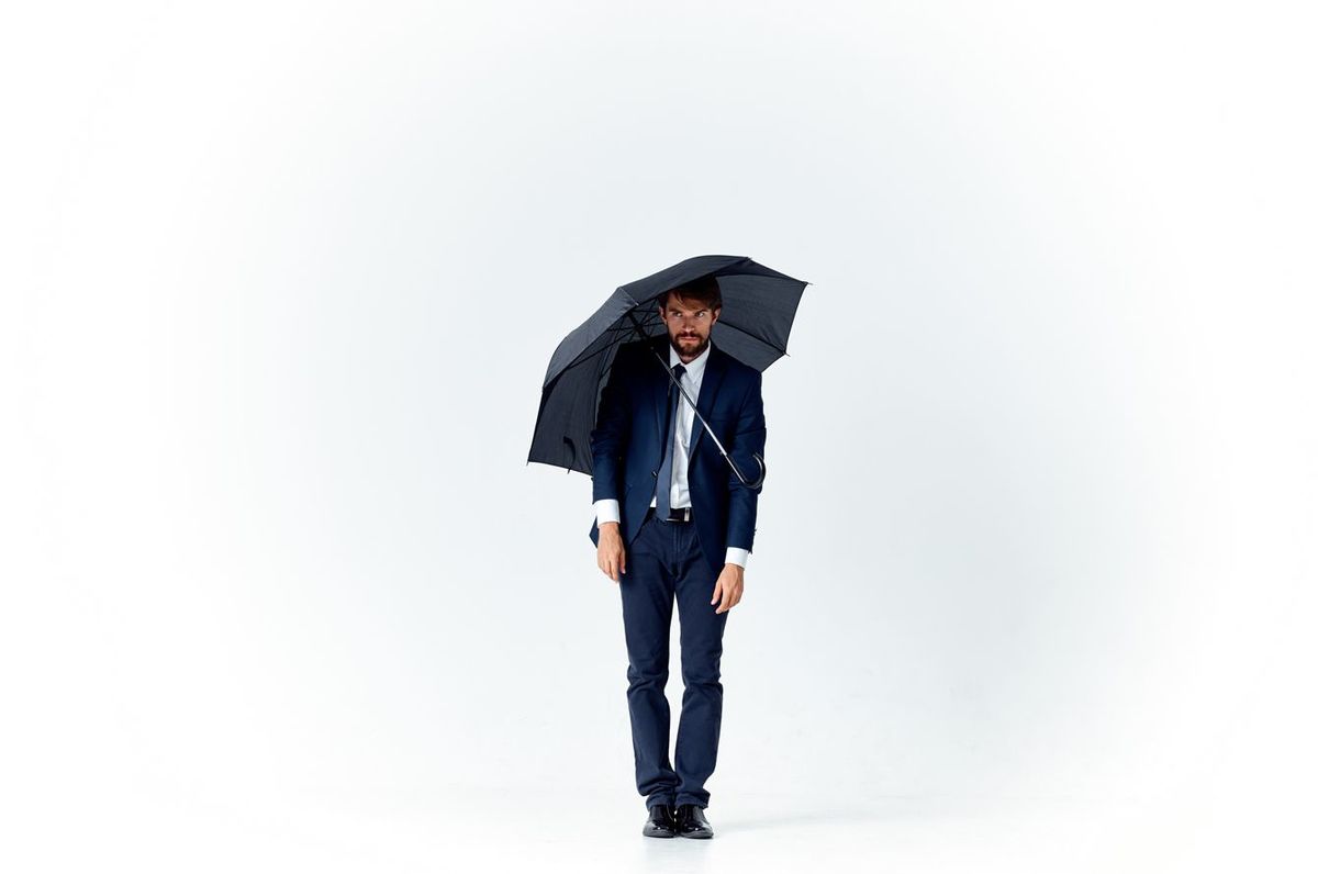 黒い傘をさし、明るい背景にスーツを着た髭を生やした男