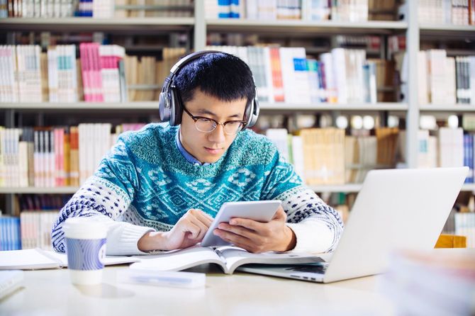 Young asian man with headset holds tablet in library