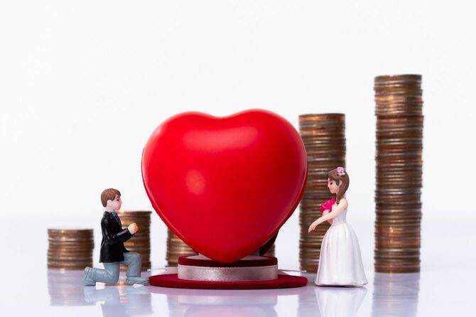 タキシードとウェディングドレスのカップルの人形、背景にハートの置物と積み上げられた硬貨