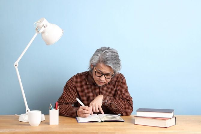 本に書き込みをしながら勉強しているシニア男性