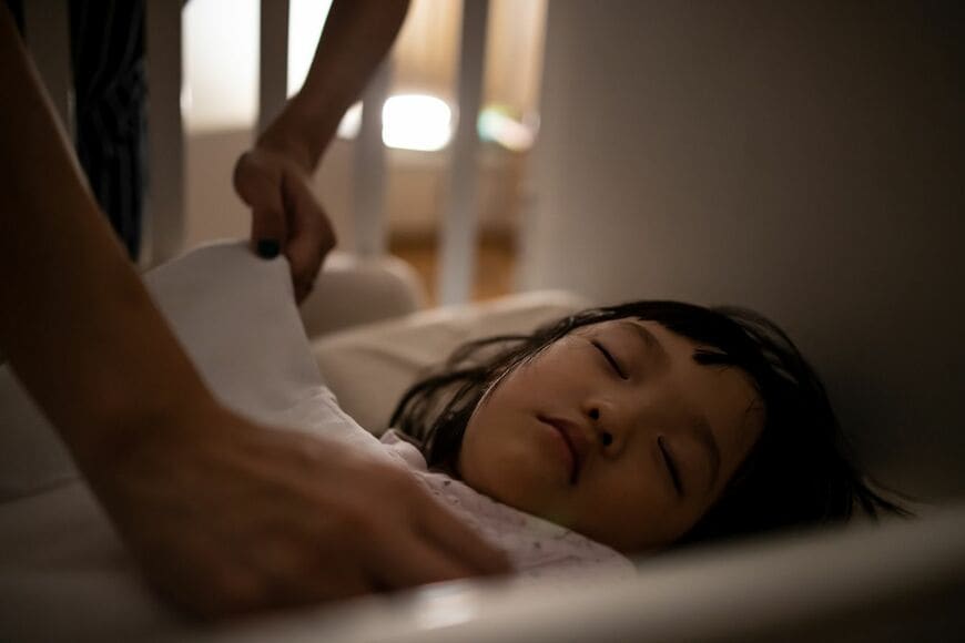 寝ている子どもの掛け布団を直している親の手