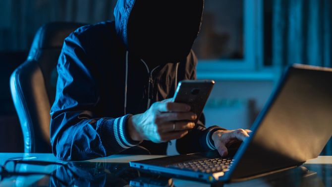 匿名のハッカーが暗闇でスマホとパソコンで何かしている
